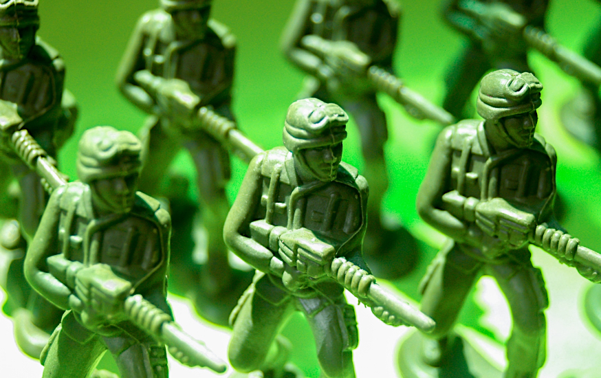 A line-up of green, plastic toy soldiers, all identical and mass-produced. The mould line is highly visible on each figure. Their uniform appears to be an odd mix of 1930s aviator and early 1990s US soldier, their 'fritz' helmets crowned with goggles. They all carry the same ray gun, a long, boxy and ribbed affair that looks almost Atompunk. Original image by icon0.com (@icon0com), c/o PublicDomainPictures (@PDpictures)